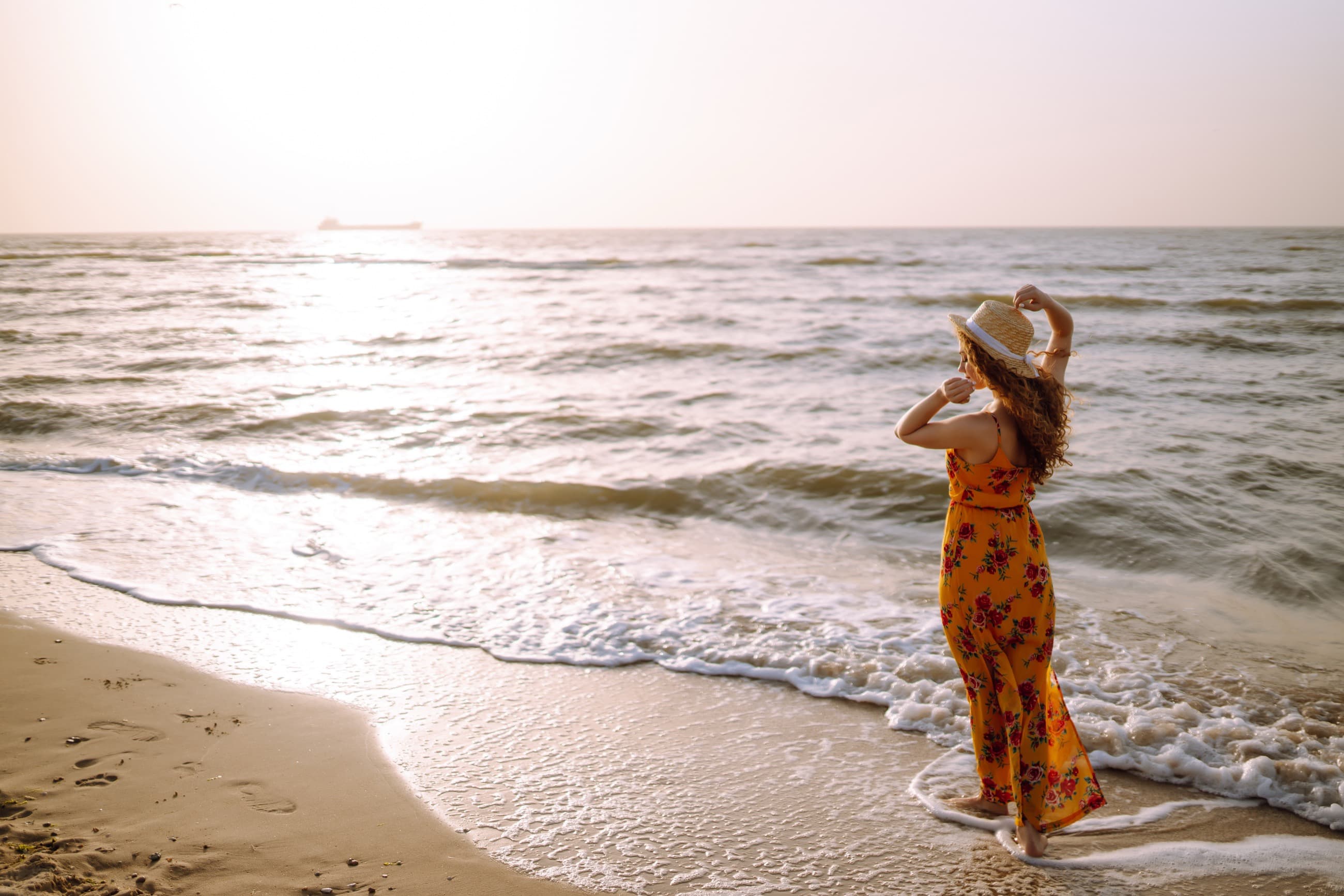 Woman in a sundress walking along the shoreline at sunset